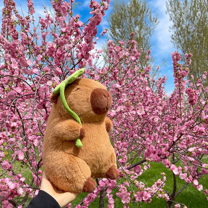 Capybara plush toy with green lotus leaf and relaxed expression